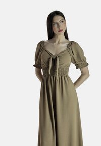 Vestito marrone smockato con una chiusura a cravatta, maniche a sbuffo e una gonna fluida. Il tessuto testurizzato aggiunge profondità, adatto sia per un abbigliamento casual che formale.
