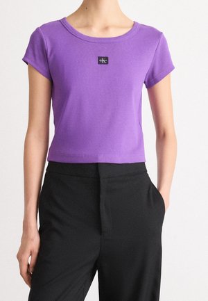Top court violet slim fit à manches courtes avec un petit patch noir du logo Calvin Klein sur la poitrine, associé à un pantalon noir taille haute.