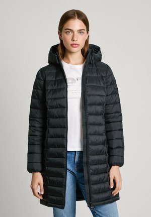 Zwarte gewatteerde jas met een capuchon, voorzien van horizontale stiksels, ritssluiting en elastische manchetten. Draagt over een wit T-shirt en blauwe spijkerbroek.