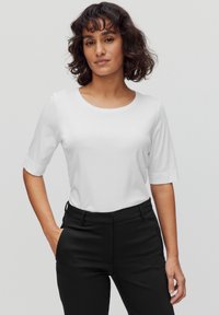 Vit kortärmad topp med rund halsringning, kombinerad med svarta byxor. Tyget verkar slätt och lätt, med en ren, minimalistisk design.