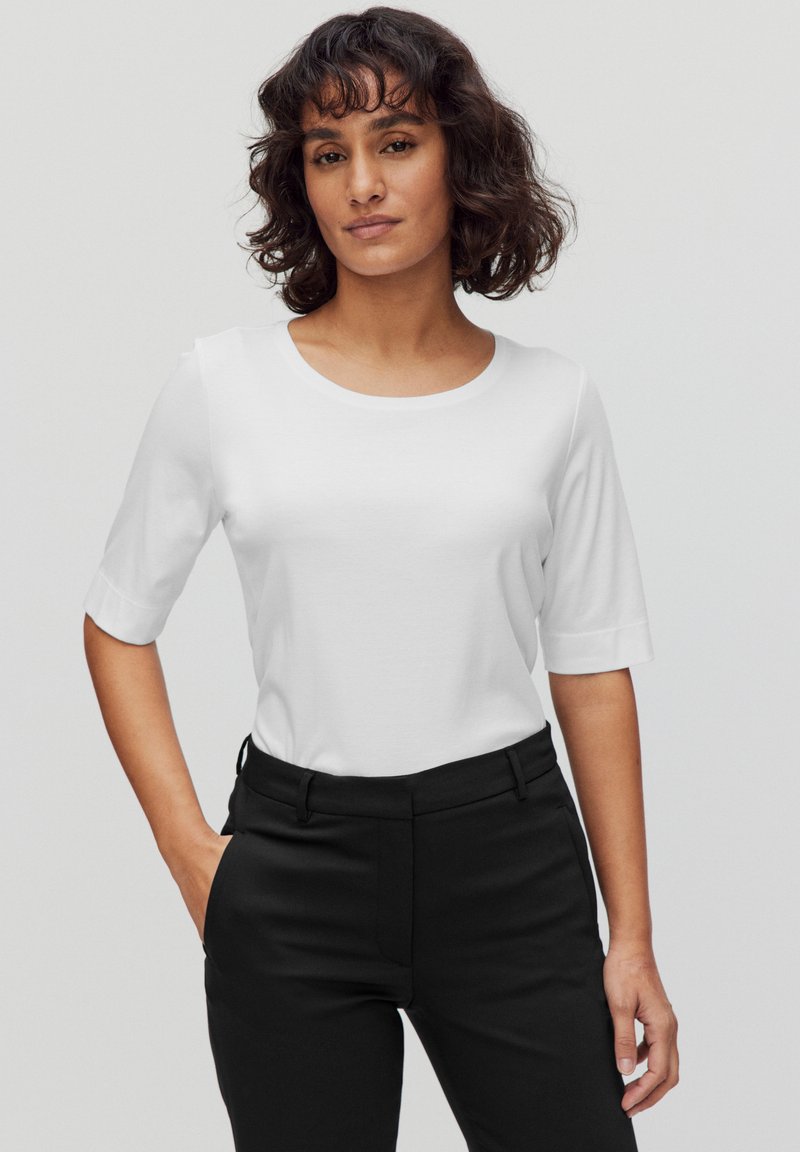 Vit kortärmad topp med rund halsringning, kombinerad med svarta byxor. Tyget verkar slätt och lätt, med en ren, minimalistisk design.