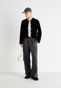 Zwarte gebreide cardigan met gouden knopen, witte geribde top, grijze broek met elastische tailleband, grijze pet en witte handtas. Zwarte schoenen.