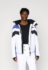 Valge ja sinine isoleeritud jakk mustade aktsentidega, kõrge kraega ja tõmblukuga. Omab stiilset disaini ja avaraid taskuid.