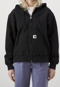 Black zip-up hoodie made of cotton blend, featuring a kangaroo pocket, drawstring hood, and ribbed cuffs. Tag visible on the front.