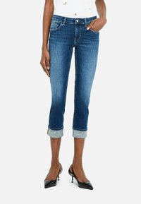 Jean capri en denim bleu moyen avec des ourlets roulés et des détails bleu clair. Design ajusté avec cinq poches et de subtils accents de couture.