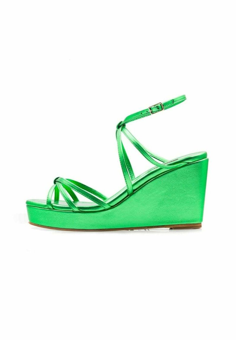Sandalias de cuña metálicas verdes con tiras cruzadas delgadas y una correa en el tobillo, con una textura suave y un alto tacón de cuña.