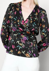 Svart blommig blus med djup V-halsringning, långa ärmar och smal midja. Har färgglada blommor i lila, rosa och gult på ett silkeslena tyg.