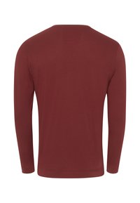 Camicia a maniche lunghe di un rosso intenso, realizzata in morbido cotone, presenta un collo a giro e polsini elastici, con una texture liscia e uniforme.