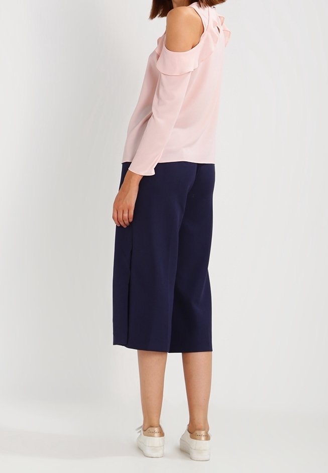 Blusa rosa pallido con spalle scoperte e dettagli a ruffle, abbinata a culottes blu navy. I pantaloni hanno una linea dritta e arrivano sotto il ginocchio.