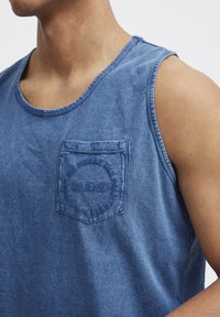 Blå denim tank top med rund hals, lomme på venstre bryst med preget tekst og en avslappet passform. Strukturert stoff med lett glans.