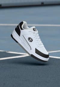 Λευκό αθλητικό παπούτσι με μαύρες λεπτομέρειες, από δέρμα και συνθετικά υλικά, διάτρητο στην περιοχή των δακτύλων, επίπεδα κορδόνια και μαλακή σόλα για υποστήριξη.