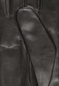 Gants en cuir noir au toucher lisse, dotés d'un design ajusté. Des détails de couture notables et des plis subtils rehaussent l'apparence naturelle.