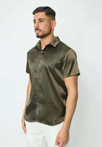 Chemise à manches courtes, verte olive, en tissu lisse ; elle présente un col classique et une fermeture à boutons avec un ourlet arrondi.