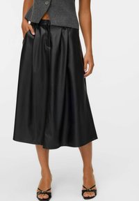 Zwarte leren midi-rok met een geplooid design, elastische tailleband en zakken. Draagt een grijze wollen vest en zwarte sandalen met bandjes.