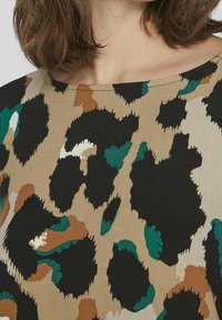 Top con stampa leopardata caratterizzato da una miscela di nero, beige e verde con macchie irregolari e textured. Tessuto morbido e ampio scollo rotondo.
