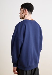 Námořnická modrá oversized mikina s kulatým výstřihem, spadlými rameny a žebrovanými manžetami. Vyrobena z m�ěkkého bavlněného materiálu s hladkou texturou.