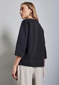 Sudadera negra con mangas tres cuartos, cuello redondo y un corte relajado. Textura suave y detalles de costura sutiles.