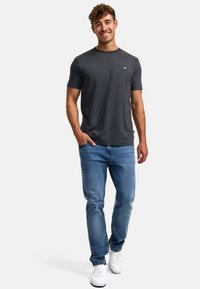 Mørk grå bomull T-skjorte med rund hals og liten blå logo på brystet, kombinert med lyse blå jeans og hvite joggesko.