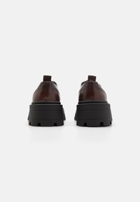 Scarpe in pelle marrone con una spessa suola piattaforma nera, dotate di punta arrotondata e di una piccola linguetta sul tallone per facilitare l'indossamento.