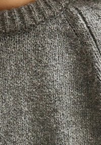 Grijze gebreide trui met een gestructureerd patroon. Voorzien van een ribbelhalslijn en naden langs de schouders. Zacht stof. Close-up weergave.