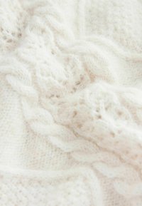Strukturierter, weißer Strickstoff mit einem Kabelmuster, weicher Erscheinung und zarter, luftiger Webart, typisch für warme Winterkleidung.