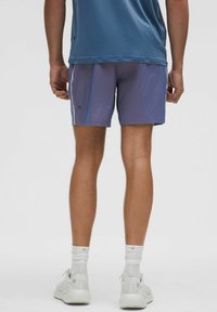 Lilla træningsshorts med en let skinnende overflade, der har sidelommer og en behagelig pasform, parret med hvide sneakers og sokker.