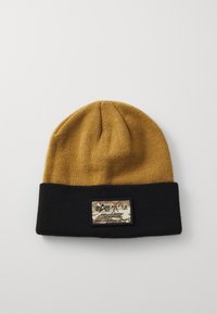 Căciulă tricotată, cu vârf de culoare maro auriu și margine neagră. Prezintă un patch de marcă dreptunghiular cu un design în camuflaj și text alb.