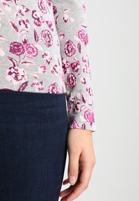 Haut gris avec motif floral violet, tissu en mélange de coton, manches longues, encolure arrondie, associé à un jean en denim foncé.
