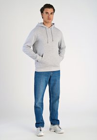 Felpa grigia in cotone con cappuccio e cordoncino, grandi tasche frontali e polsini a costine, abbinata a jeans blu e sneakers bianche.