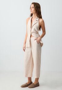 Lichtbeige linnen mouwloze blazer met een diepe V-hals, gecombineerd met bijpassende brede broekspijpen. Glad textuur, minimalistisch ontwerp.