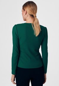 Zielona, prążkowana bluzka z długim rękawem o dopasowanym kroju i subtelnymi fałdami na ramionach, z okrągłym dekoltem i gładką fakturą.