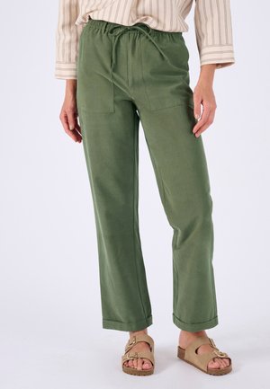 Lichtgroene, losse broek met een trekkoord in de taille, zijzakken en omgeslagen zoom. Gemaakt van zacht materiaal. Draagt beige sandalen.