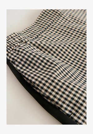 Tissu à carreaux noir et beige avec une surface texturée, présentant un fronces élastique en haut et une bordure noire unie en bas.