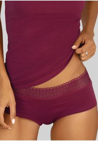 Burgundy bomuldsshorts med en detaljeret blonde i taljen; blød tekstur og tætsiddende design. En matchende tanktop, også i burgunder, er delvist synlig.