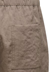 Braune Stoffhosen mit strukturiertem Oberflächenmaterial, elastischem Bund und einer seitlichen aufgesetzten Tasche.