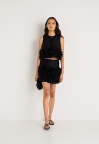 Conjunto coordenado preto composto por um top sem mangas e uma mini saia com detalhe floral texturizado ao longo da bainha. Tecido suave com uma silhueta ajustada.