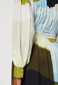 Monivärinen mekko, jossa on liukuvärjätty kuvio, jossa on kermaa, sinistä, vihreää ja ruskeaa. Mekossa on pullistetut hihat ja rypytetty vyötärönauha, jossa on nappikoristeita.