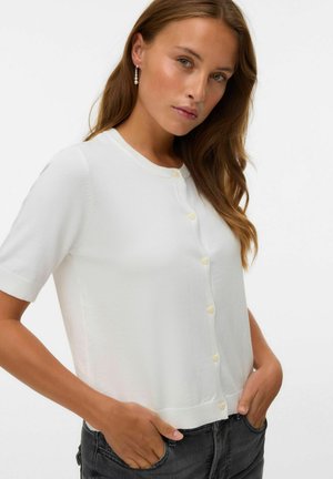 White short-sleeve cardigan with round neckline, textured fabric, and light yellow button detailing, paired with gray jeans.