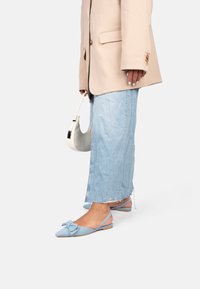 Himmelblaues Slingback-Balletschuh-Modell mit einer Schleifendekoration, kombiniert mit einem beigen übergroßen Blazer und einem ausgefransten blauen Jeansrock. Akzentuiert durch eine weiße Tasche.