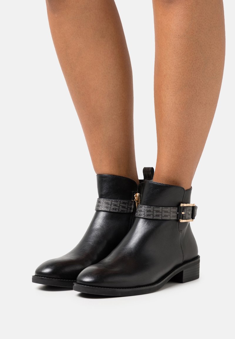 Bottes mi-mollet en cuir noir avec un bout rond, dotées d'une sangle grise texturée et d'une boucle dorée en accent. Conçues avec un talon bloc bas.