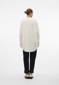 Oversized cream sweater with long sleeves, ribbed hem, and rounded back. Paired with black rolled-up pants and light footwear.