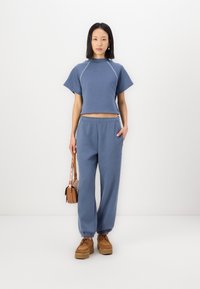 Hellblau geschnittenes Sweatshirt mit kurzen Ärmeln und kontrastierenden Nähten, kombiniert mit passenden lockeren Sweatpants und braunen Plattform-Sneakern.
