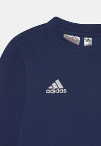 Camisa de manga larga azul marino con cuello redondo, que presenta un logotipo de Adidas bordado en blanco en el lado izquierdo del pecho y una textura de tela suave.
