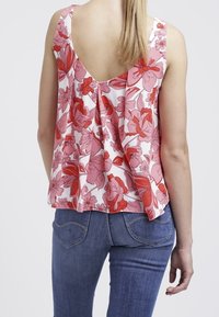 Top senza maniche floreale con schiena profonda, caratterizzato da motivi floreali rosa e rossi su sfondo bianco; abbinato a jeans blu.