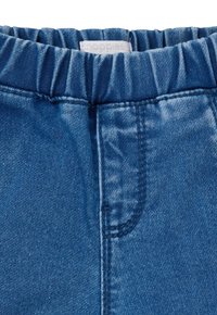 Denim broek met een zachte elastische tailleband, uitgevoerd in een klassieke vijfzakkenontwerp in een middelblauwe wassing met subtiele textuurvariaties.