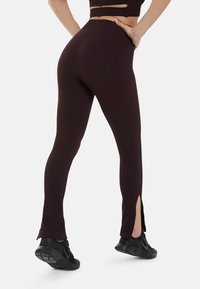 Bordeaux geribbelde leggings met slits bij de enkels, hoog in de taille, gecombineerd met zwarte sportschoenen. Zachte textuur en aansluitende pasvorm.