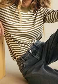 Vihreävalkoinen raidallinen pitkähihainen paita, jossa on ribbaus pääntiellä, yhdistettynä korkeavyötäröisiin tummansinisistä denimiin. Pehmeä kangas, rento istuvuus.