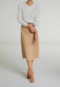 Ljusgrå ribbad tröja med puffärmar, i kombination med en beige läder midi kjol som har en sidofåra och en slät textur. Tan sandaler med remmar.