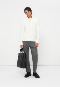 White zip-neck sweater paired with gray tailored trousers. Black leather tote bag with vertical seams, worn with black dress shoes.