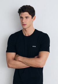 Schwarzes Baumwoll-T-Shirt mit kurzen Ärmeln, mit einem weißen "BOSS"-Logo auf der linken Brust. Glatte Textur und klassischer Rundhalsausschnitt.